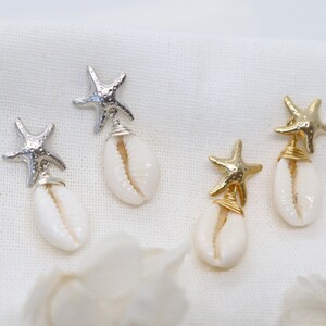 Può includere: Due paia di orecchini pendenti con un ciondolo a forma di stella marina metallica fissato a una conchiglia di ciprea bianca. Un paio ha stelle marine argentate con filo d'argento, l'altro ha stelle dorate con filo d'oro.