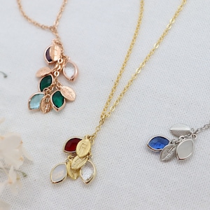 Könnte beinhalten: Drei zarte Halsketten mit Anhängern in Form von Blättern und Edelsteinen. Die Halsketten sind in Gold, Silber und Roségold. Die Anhänger sind in verschiedenen Farben, darunter Grün, Blau, Rot und Weiß.