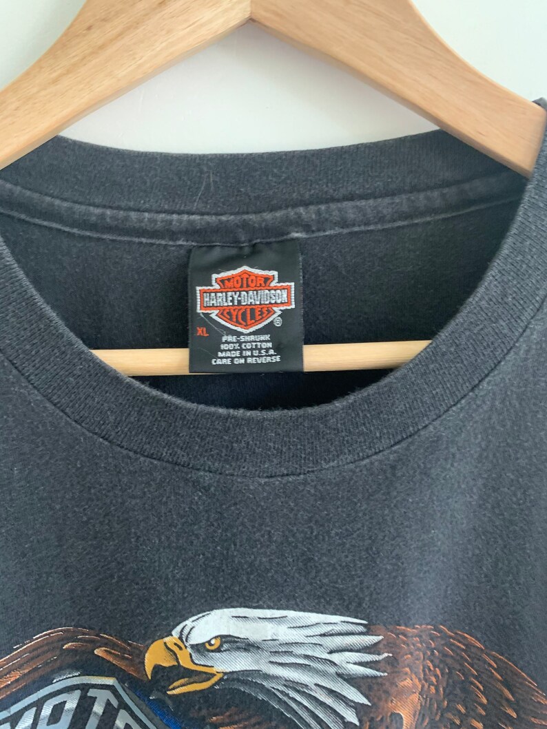 May include: Black t-shirt with a Harley-Davidson logo and an eagle graphic. The tag says "Pre-shrunk 100% Cotton Made in U.S.A. Care on Reverse".