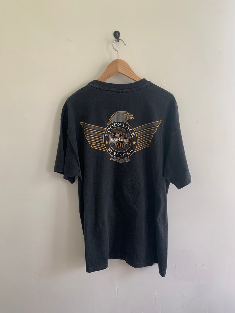 May include: Black t-shirt with a graphic of a winged eagle and the text "Woodstock Motor Harley Davidson Cycles New York Since 1975"