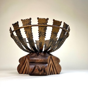 May include: A decorative bowl made of metal with a hammered finish and a wooden base. The bowl is shaped like a flower with petals that curve upwards. The base is carved with a geometric pattern.