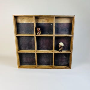 May include: A wooden display case with nine compartments. The case has a dark brown finish and is made of wood. Two small wooden figurines are displayed in the case.