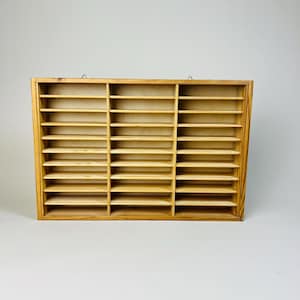 Op de afbeelding: Een houten wandrek met 24 vakken om kleine spullen in op te bergen. Het rek is gemaakt van lichtbruin hout en heeft een eenvoudig ontwerp.