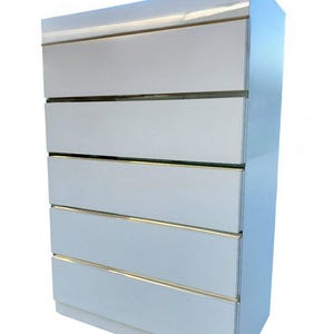 May include: A white dresser with six drawers and gold-colored trim. The top of the dresser has a curved design. The dresser is a modern piece of furniture.