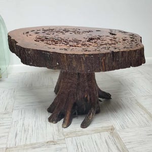 May include: A rustic, handcrafted wooden side table. The table features a natural, irregular edge and a dark brown finish. The base is made from a tree trunk, giving it a unique, organic look. The table is approximately 24 inches in diameter and 18 inches tall.