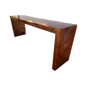 May include: A long, rectangular, wooden table with a curved top. The table is made of a dark wood with a natural finish. The table is supported by two legs on each end.