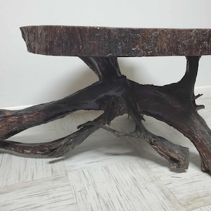 May include: A rustic, handcrafted coffee table made from a section of a tree trunk. The tabletop is a dark brown, circular shape, supported by a complex base of intertwined, dark brown tree roots. The table is approximately 30 inches long.