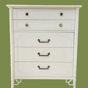 May include: A white chest of drawers featuring a faux bamboo frame design. The piece includes two smaller top drawers with round knobs and three larger lower drawers with dark metal rectangular pulls, all accented by raised bamboo-style molding.