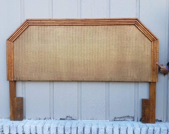 May include: A wooden headboard with a woven rattan panel. The headboard has a rounded top and is supported by two wooden legs.