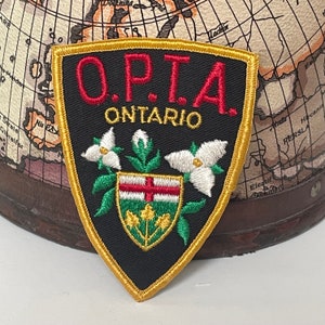 May include: A black and gold embroidered patch with the text "O.P.T.A. ONTARIO" and a stylised white trillium flower design.