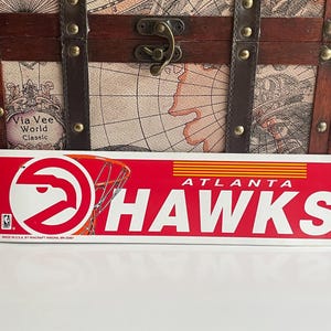 Könnte beinhalten: Roter, weißer und orangefarbener Atlanta Hawks-Aufkleber mit einem Basketballkorb und dem Logo des Teams. Der Aufkleber wird in den USA von Wincraft hergestellt.