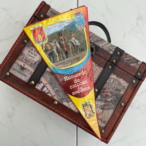 May include: A vintage-style wooden chest with a map design and metal accents. A triangular pennant with the text "Recuerdo de CALLOSA de ENSARRIA" and an image of people riding donkeys is placed on top. The pennant has yellow, red, and blue colors.