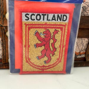 May include: An embroidered patch featuring the Scottish national flag, with the words "SCOTLAND" in white lettering and a red lion rampant on a gold shield.