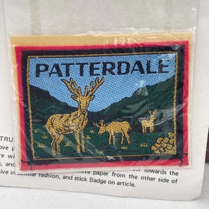 May include: Embroidered patch with the word "PATTERDALE" at the top. The patch features a blue sky, green hills, and three deer in gold and brown. The patch has a red border.