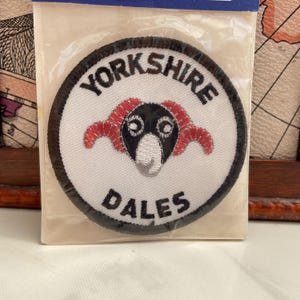 以下が含まれることがあります： 白地に黒で「Yorkshire Dales」と刺繍された丸いパッチ。赤い角と黒い顔の雄羊の頭が特徴です。パッチは透明なプラスチックパッケージに入っています。