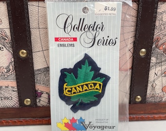 Puede incluir: Un parche de la "Collector Series" con una hoja de arce verde y la inscripción amarilla "CANADA" sobre un fondo azul oscuro. El parche está en un embalaje de plástico transparente. También se ve el texto "CANADA EMBLEMS".