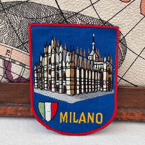 Op de afbeelding: Een blauwe geborduurde patch met een gedetailleerde afbeelding van de Dom van Milaan in wit en beige garen. Onder de kathedraal bevindt zich een klein schild met groene, witte en rode strepen en de gele tekst MILANO onderaan geborduurd.