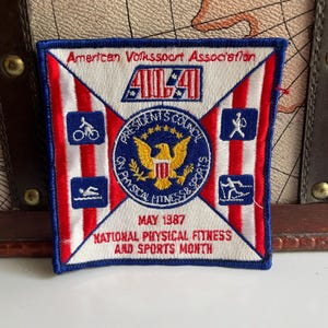 May include: A square patch with a blue border, featuring the text "American Volkssport Association" and "National Physical Fitness and Sports Month." It includes a central emblem with an eagle and the text "President's Council on Physical Fitness & Sports."