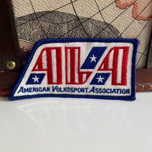 May include: Embroidered patch with a blue border and the text "ALA" in red and white, with blue sections containing white stars. The text "AMERICAN VOLKSSPORT ASSOCIATION" is below the main text.