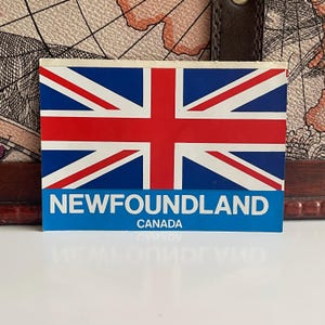 May include: A blue and white sticker with a red, white, and blue Union Jack flag. The sticker says "NEWFOUNDLAND CANADA" in white letters on a blue background.