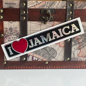 May include: A white sticker with a red heart and the text "I love Jamaica" in black letters. The sticker has a holographic finish.