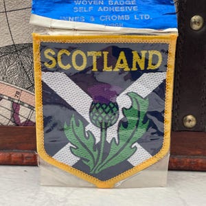 May include: A white ceramic mug with a black handle and the text "But First, Coffee" in a bold, black font. The mug is filled with a dark liquid, likely coffee, and sits on a light-colored surface.