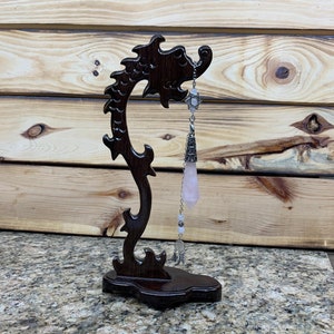May include: A pink crystal pendulum hanging from a silver chain on a dark wood dragon-shaped stand.