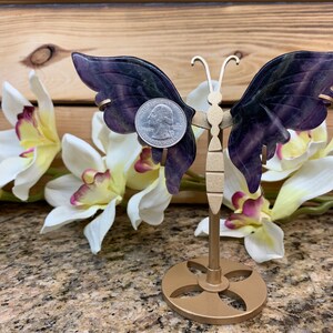 May include: A purple and green fluorite butterfly sculpture on a gold metal stand. The butterfly is about the size of a US quarter.