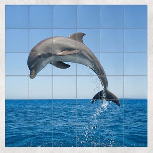 May include: A gray dolphin leaps out of the blue water, its body arched in mid-air. The dolphin's tail is visible as it breaks the surface of the water, creating a spray of water droplets.