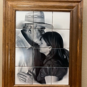 May include: A black and white photo of a man and woman in a framed tile mosaic. The man is wearing a cowboy hat and a plaid shirt. The woman is wearing a dark shirt. The man is kissing the woman on the forehead.