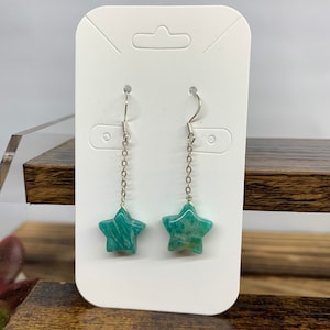 May include: A pair of silver star-shaped earrings with green aventurine stone. The earrings are on a white card.