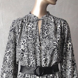 Peut inclure: Une robe à imprimé animal blanc et noir à manches longues et une ceinture noire. La robe a un décolleté en forme de trou de serrure et un ourlet à volants.