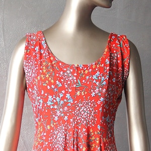 Peut inclure: Une robe rouge sans manches avec un imprimé floral. La robe a un col rond et un corsage ajusté. La jupe est ample et fluide.