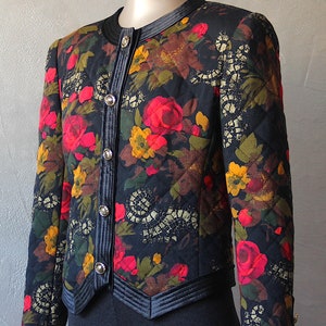 May include: A black quilted jacket with a floral print featuring red, yellow, and green flowers. The jacket has a velvet trim and gold buttons.