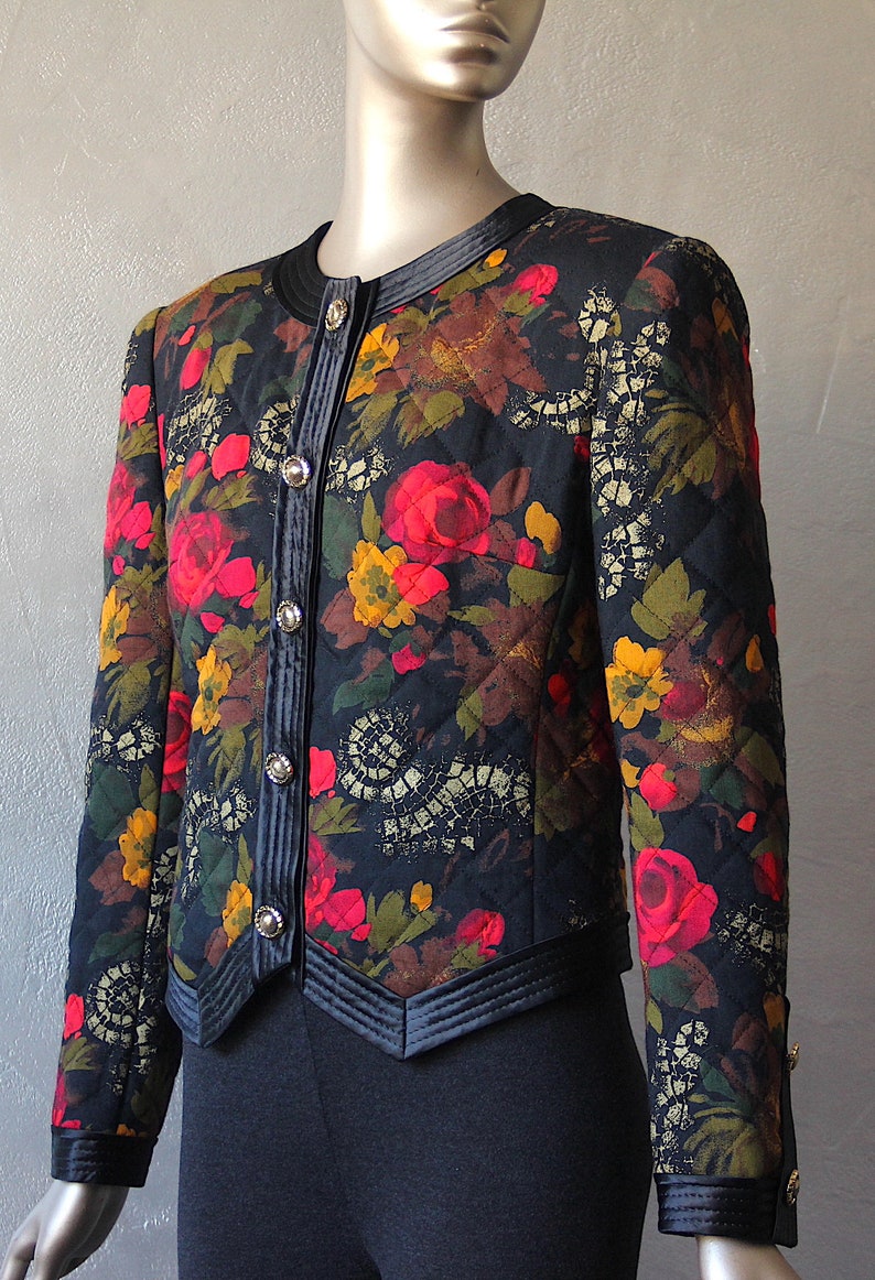 May include: A black quilted jacket with a floral print featuring red, yellow, and green flowers. The jacket has a velvet trim and gold buttons.