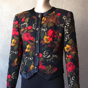 May include: A black quilted jacket with a floral print featuring red, yellow, and green flowers. The jacket has a satin trim and gold buttons.