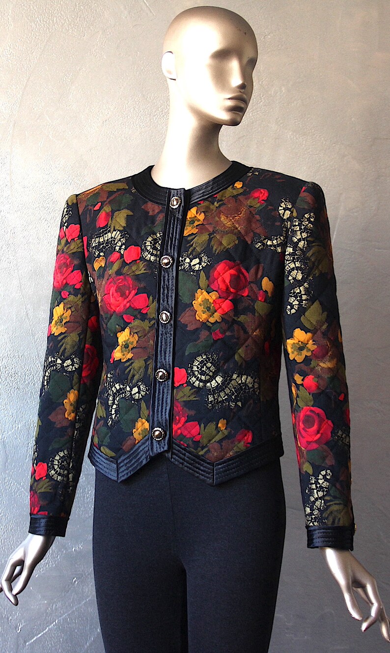 May include: A black quilted jacket with a floral print featuring red, yellow, and green flowers. The jacket has a satin trim and gold buttons.