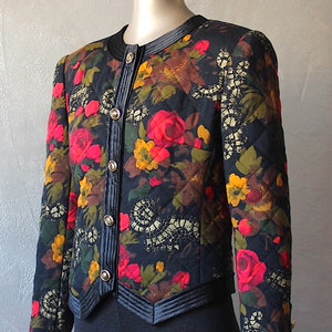 May include: A black quilted jacket with a floral print featuring red, yellow, and green flowers. The jacket has a black velvet collar and a button closure.