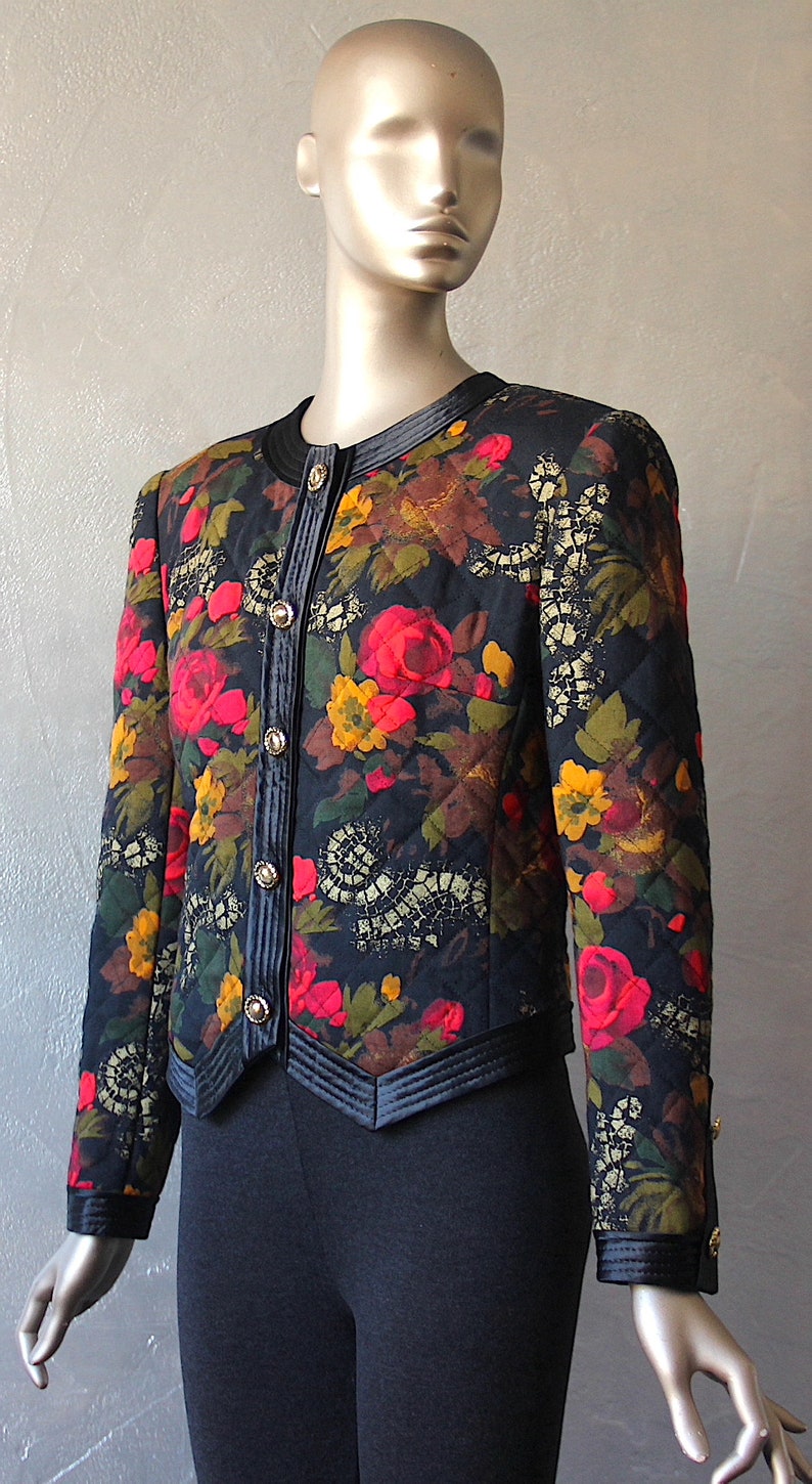 May include: A black quilted jacket with a floral print featuring red, yellow, and green flowers. The jacket has a black velvet collar and a button closure.