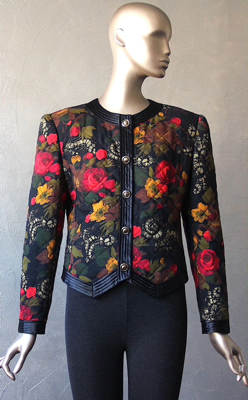May include: A black quilted jacket with a floral print featuring red, yellow, and green flowers. The jacket has a black velvet collar and trim, and silver buttons down the front.