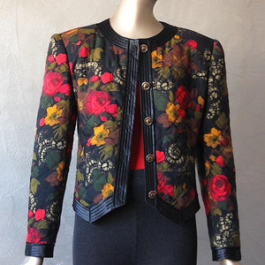 May include: A black quilted jacket with a floral print featuring red, yellow, and green flowers. The jacket has a black velvet trim and gold buttons.