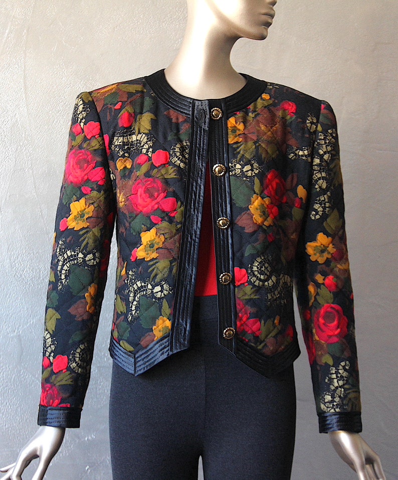 May include: A black quilted jacket with a floral print featuring red, yellow, and green flowers. The jacket has a black velvet trim and gold buttons.