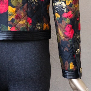 May include: A black quilted jacket with a floral print in shades of red, yellow, and brown. The jacket has a black satin trim and gold buttons on the cuffs.