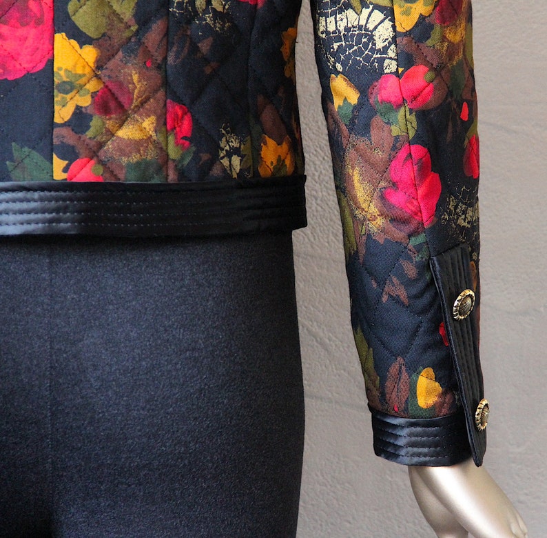 May include: A black quilted jacket with a floral print in shades of red, yellow, and brown. The jacket has a black satin trim and gold buttons on the cuffs.