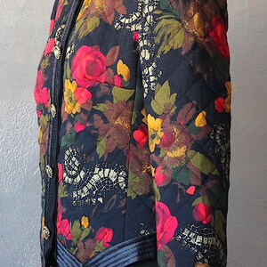 May include: A black quilted jacket with a floral print featuring red, yellow, and green flowers. The jacket has a black collar, black trim, and gold buttons.