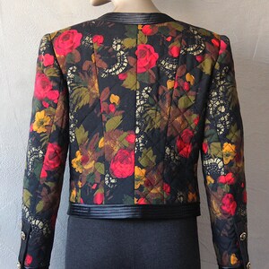 May include: A black quilted jacket with a floral print featuring red, yellow, and green roses. The jacket has a black satin collar and trim.