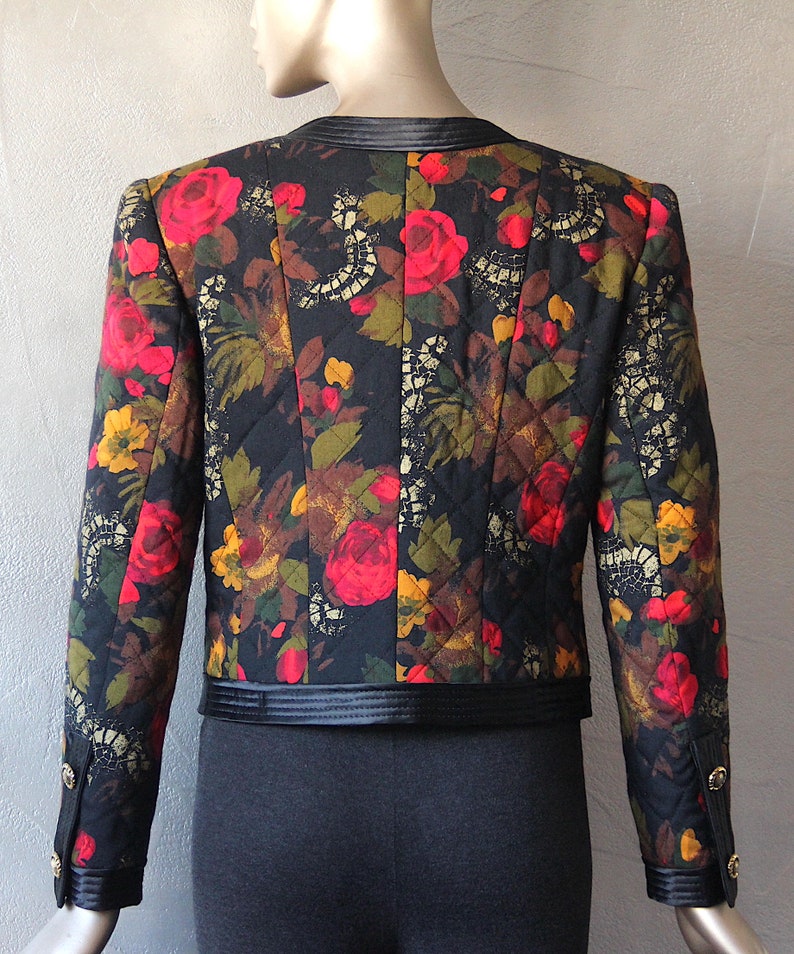 May include: A black quilted jacket with a floral print featuring red, yellow, and green roses. The jacket has a black satin collar and trim.