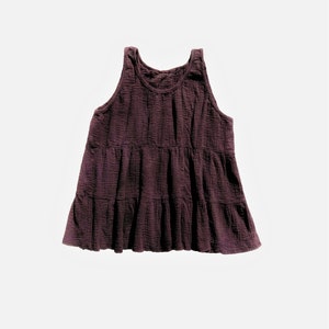 Puede incluir: Un vestido sin mangas de color burdeos oscuro con volantes. El vestido está hecho de una tela suave y texturizada y tiene un corte holgado.