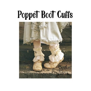 May include: A pair of cream-colored boot cuffs with lace trim and a button detail. The cuffs are worn over white socks and brown boots. The image is captioned "Poppet Boot Cuffs" and "Opal Annie".