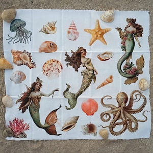 May include: A white fabric panel featuring a printed collage of three mermaids, a brown octopus, a blue jellyfish, a yellow starfish, and various seashells including conch, scallop, and spiral shells, all arranged on a sandy surface.